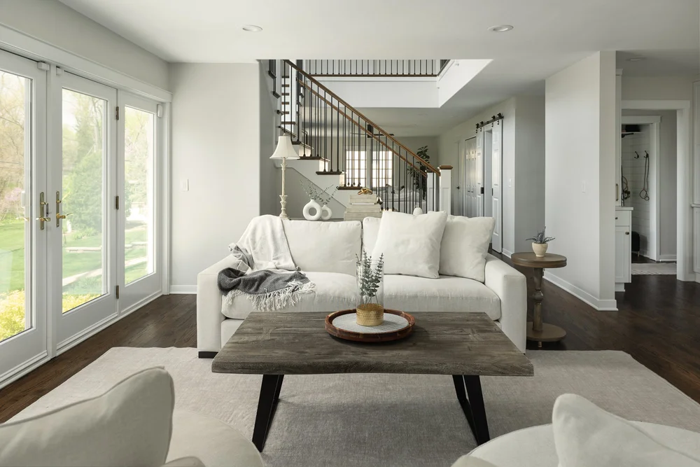 Remodeled living room with a reworked layout, neutral furnishings, and an open staircase within the existing home