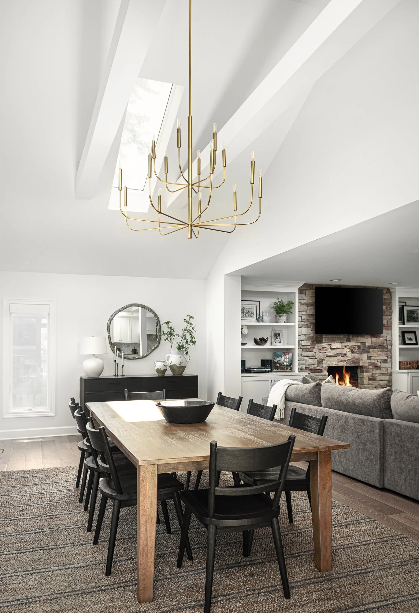 Remodeled dining room with brass chandelier opening to a living room with stone fireplace by Redstart Construction