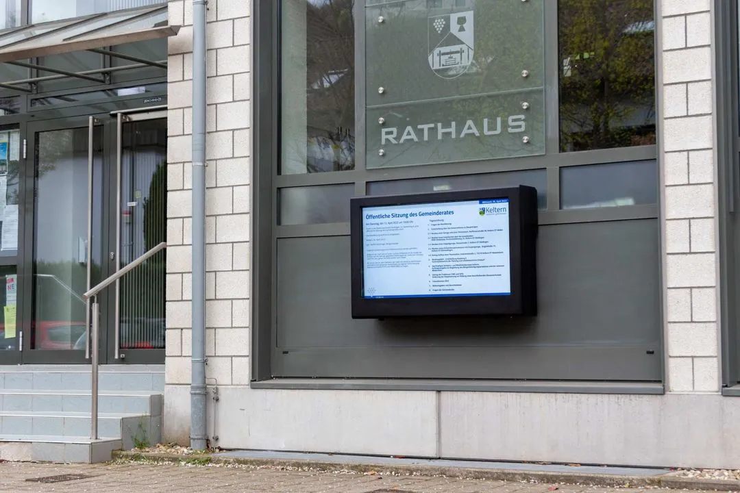Eingang zum Rathaus mit digitalem Informationsdisplay an der Wand neben der Tür.