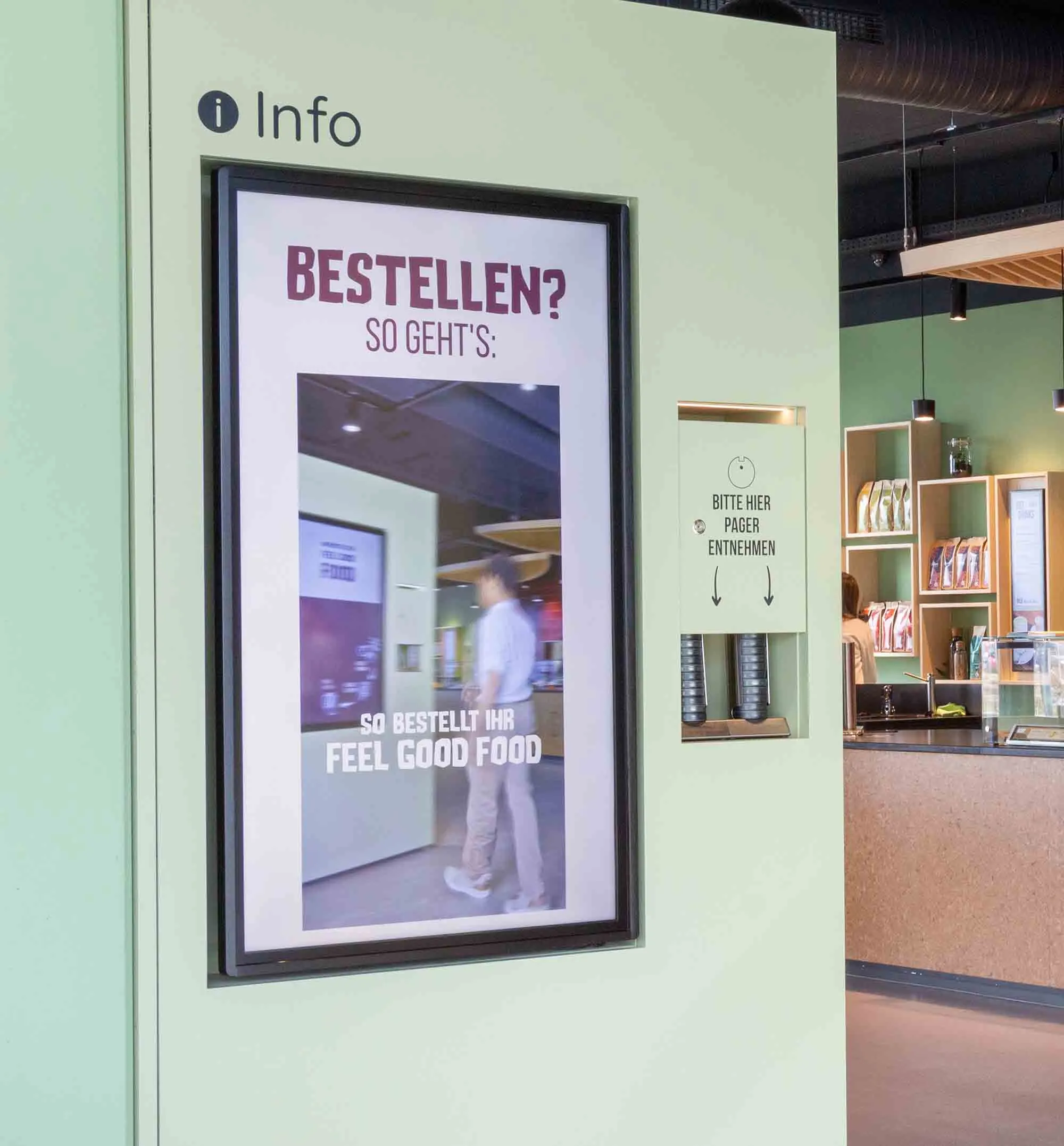 Digitales Informationsdisplay in einem Restaurant mit Anweisungen zum Bestellen von Feel Good Food und einem Bereich zum Entnehmen von Pagern.