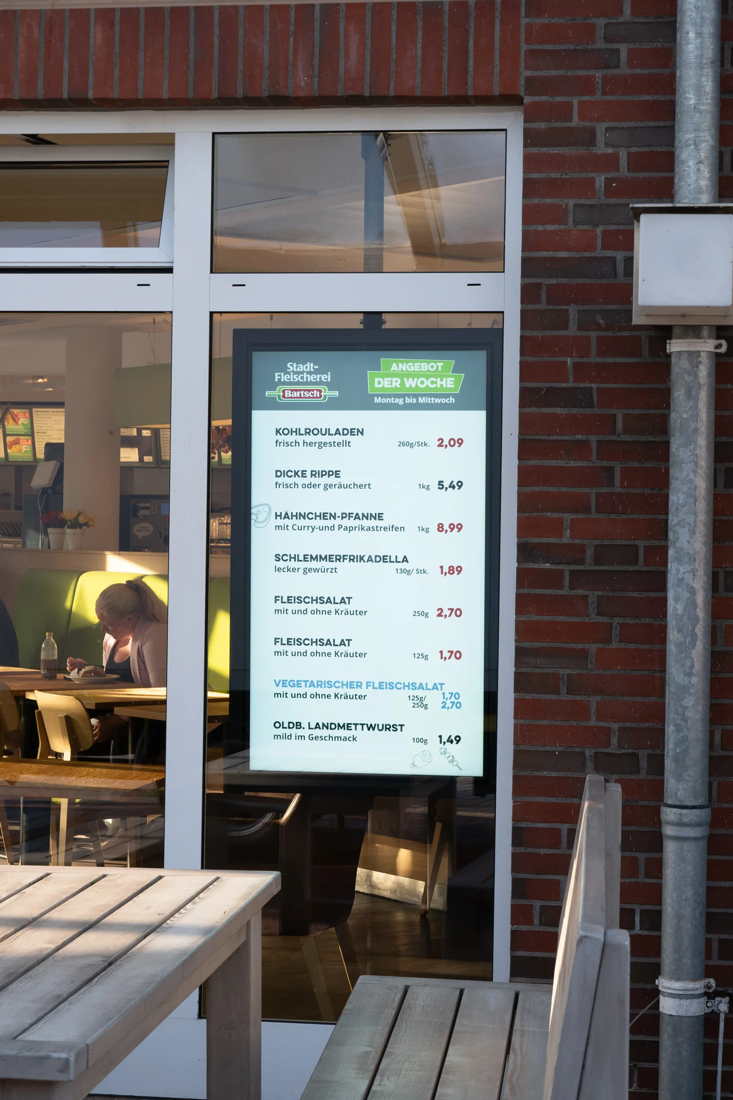 Schaufenster der Stadt-Fleischerei Bartsch mit einem digitalen Angebotsplakat der Woche für verschiedene Fleisch- und Wurstprodukte.