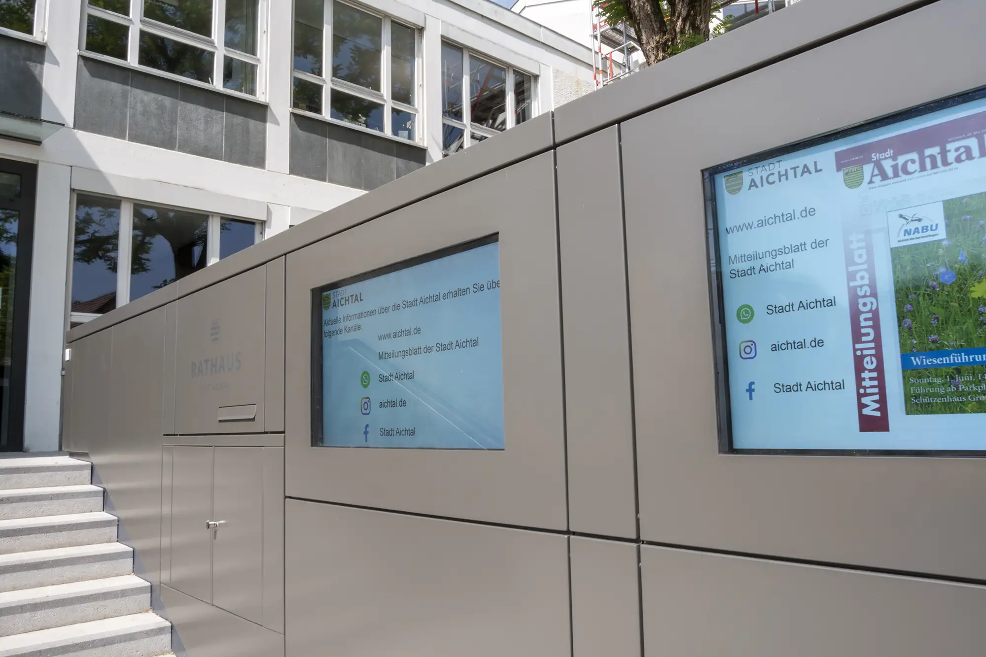 Digitales Informationsdisplay am Rathaus der Stadt Aichtal mit Links zu Website und sozialen Medien.