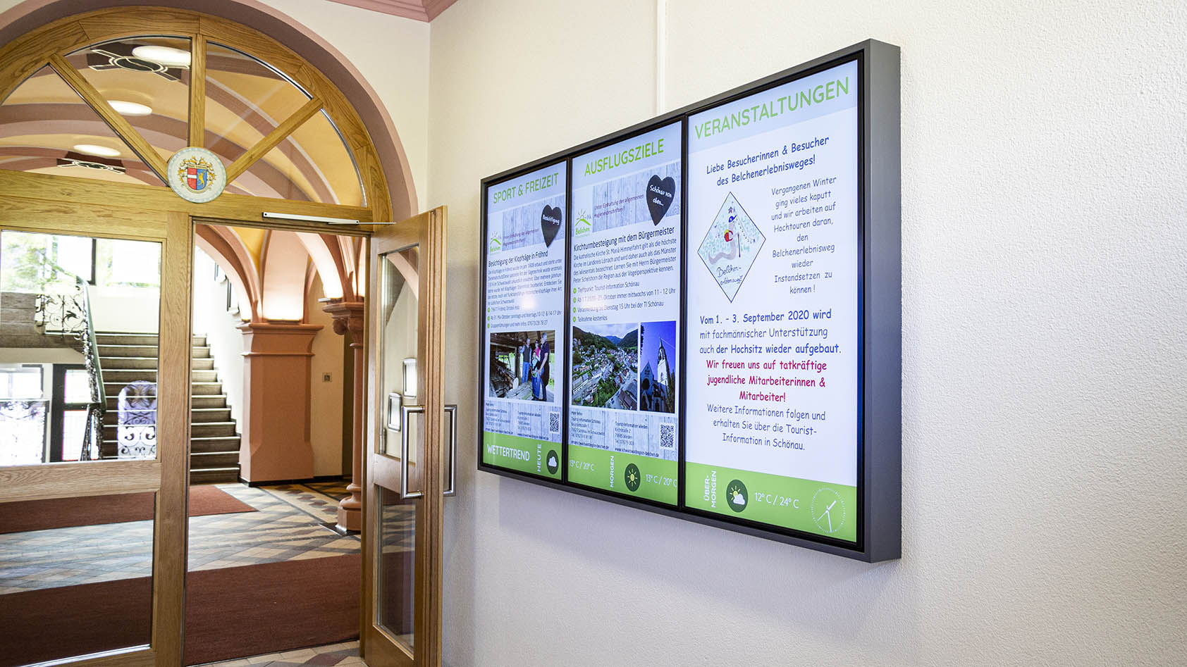 Digitale Informationsanzeige mit Wettertrend, Ausflugszielen und Veranstaltungen in einem historischen Gebäudeeingang.