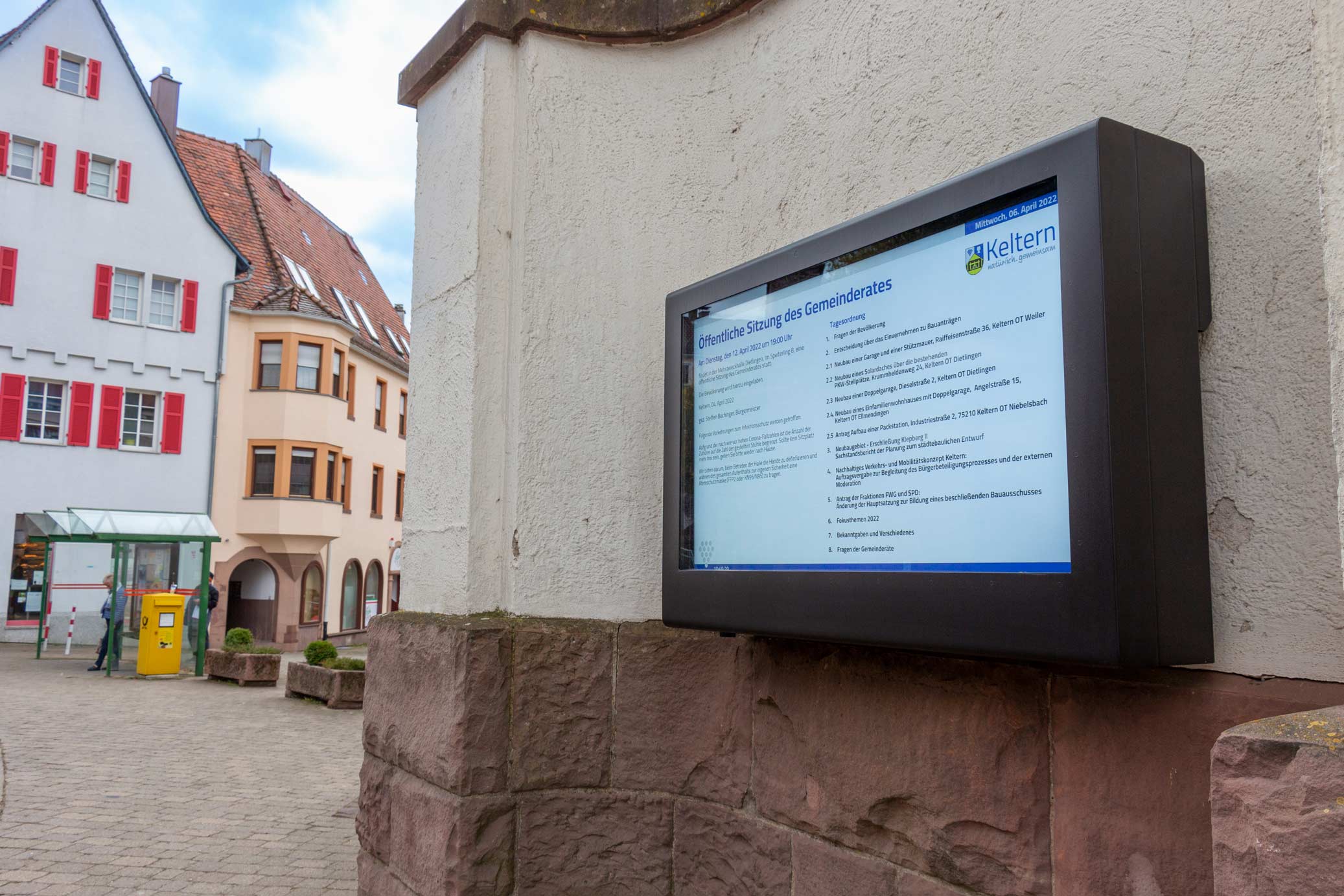 Digitale Informationstafel mit Tagesordnung einer öffentlichen Sitzung des Gemeinderates in Keltern, angebracht an einer Außenmauer eines Gebäudes im historischen Ortszentrum.