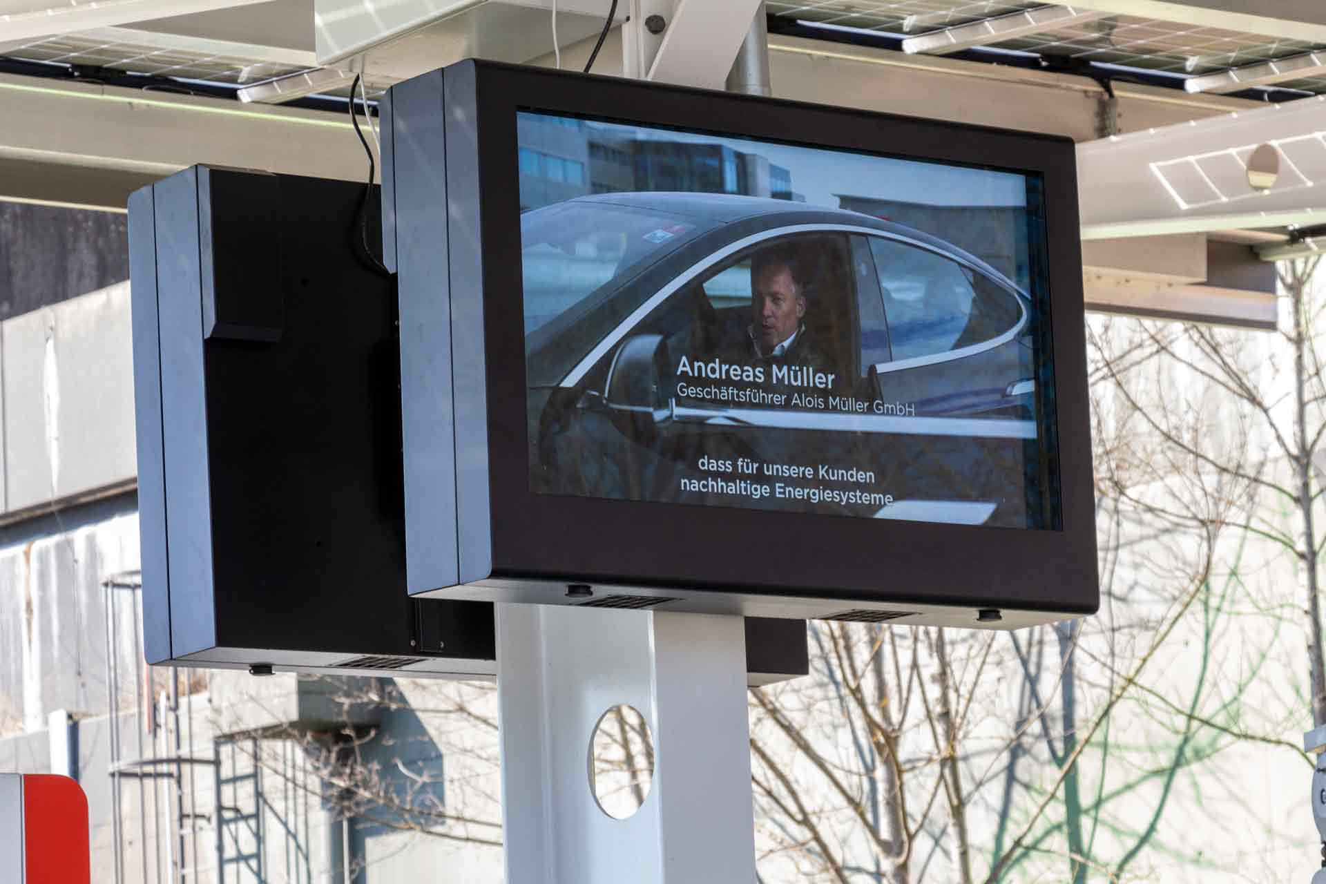 Digitale Anzeigetafel zeigt Andreas Müller im Auto mit Text über nachhaltige Energiesysteme.