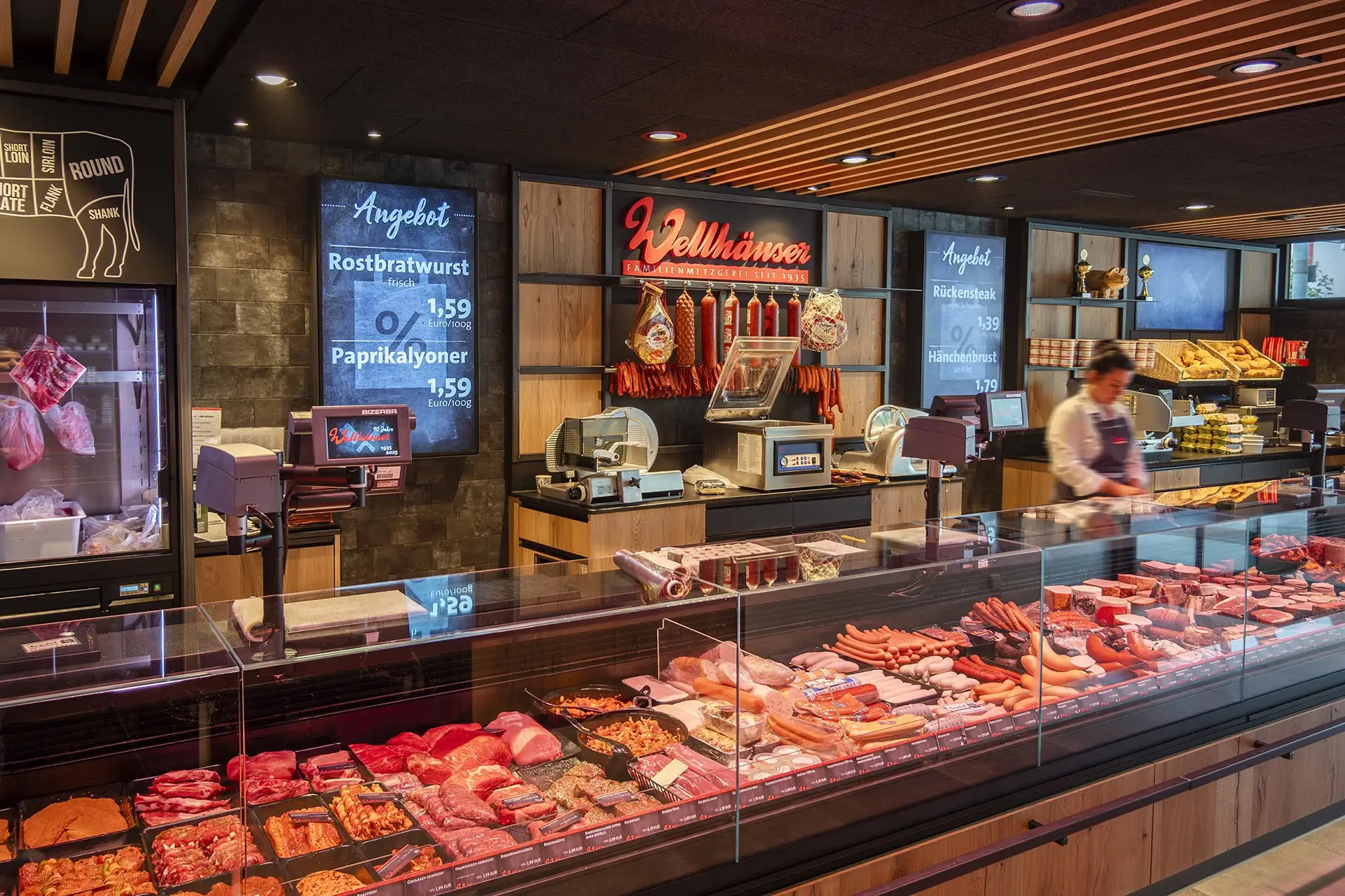 Fleischerei mit einer großen Auslage verschiedener frischer Fleisch- und Wurstwaren, dahinter eine Verkäuferin am Tresen.