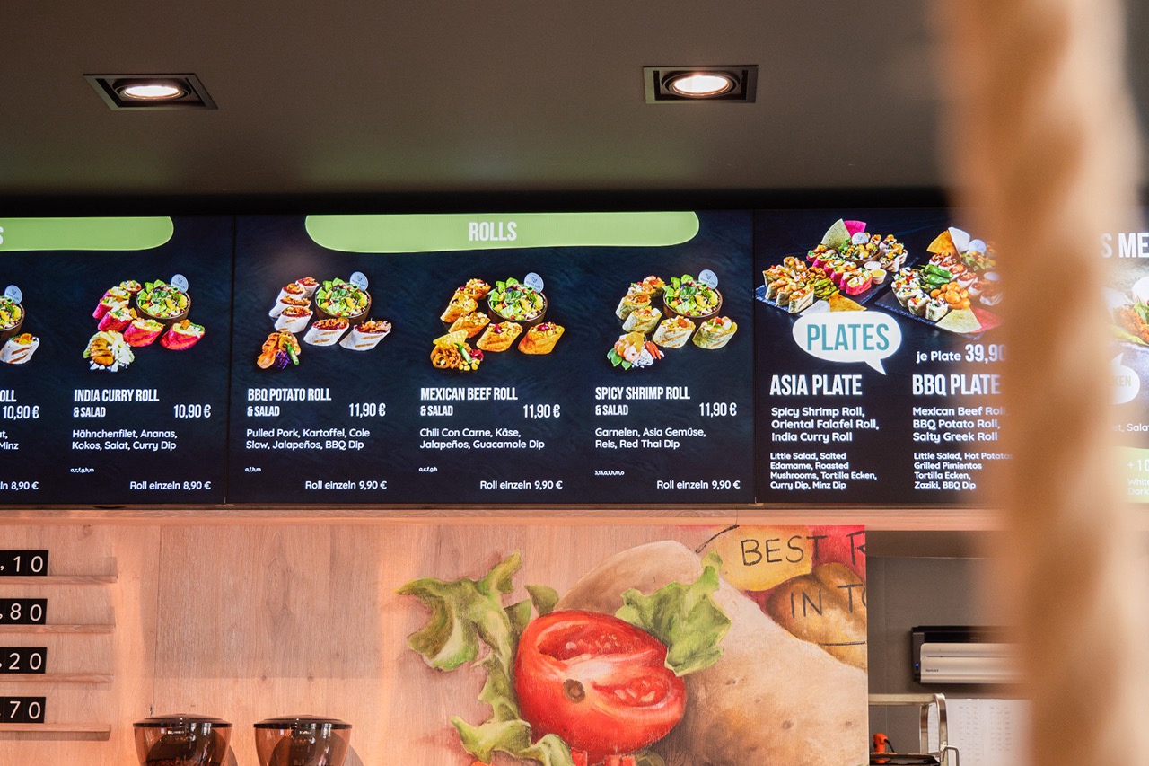 Digitales Menü mit Bildern und Preisen für verschiedene Wrap-Rollen und asiatische Tellergerichte in einem Restaurant.