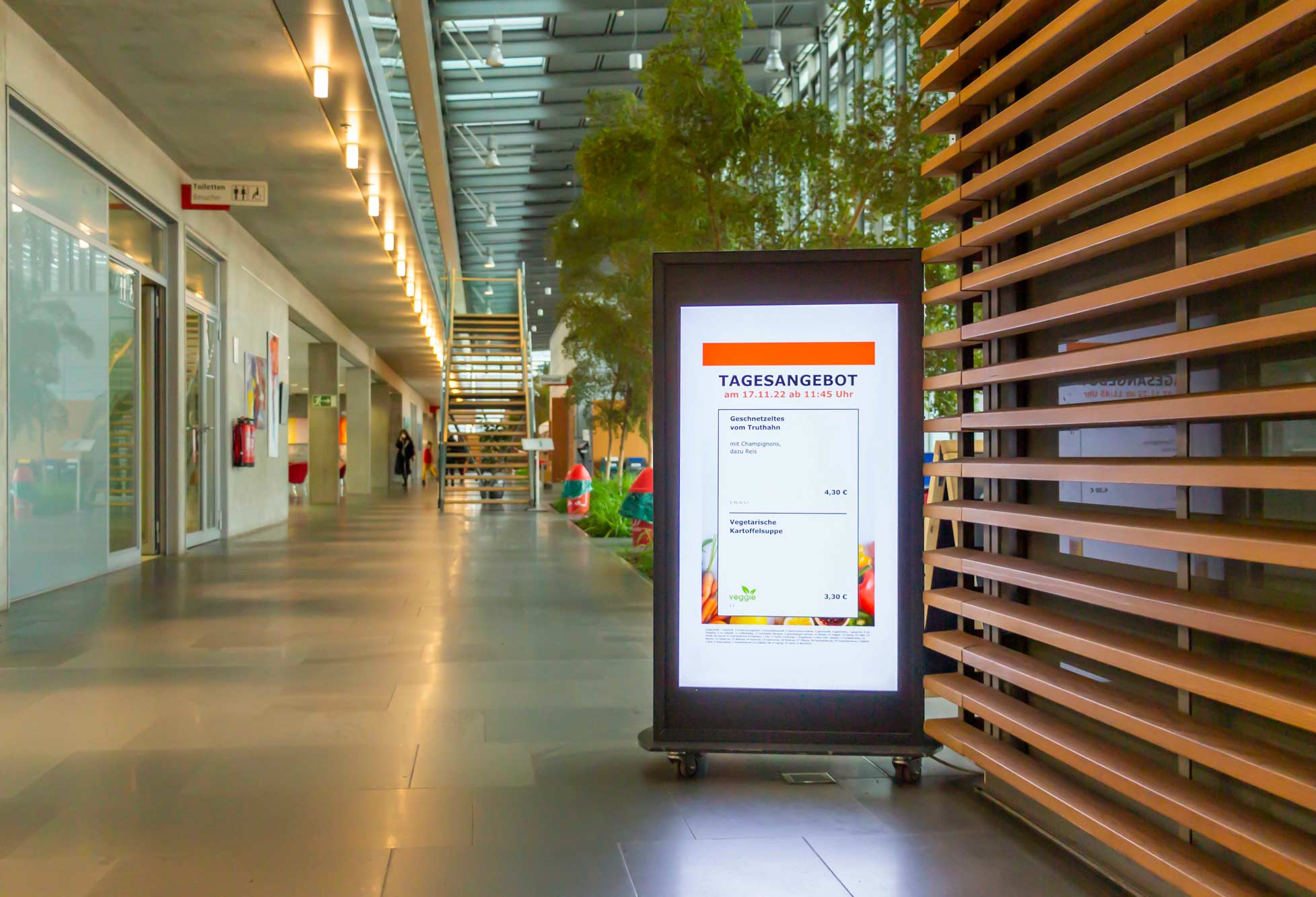 Digitales Menü-Display im Flur eines modernen Gebäudes zeigt das Tagesangebot mit Geschnetzeltem vom Truthahn und vegetarischer Kartoffelsuppe.