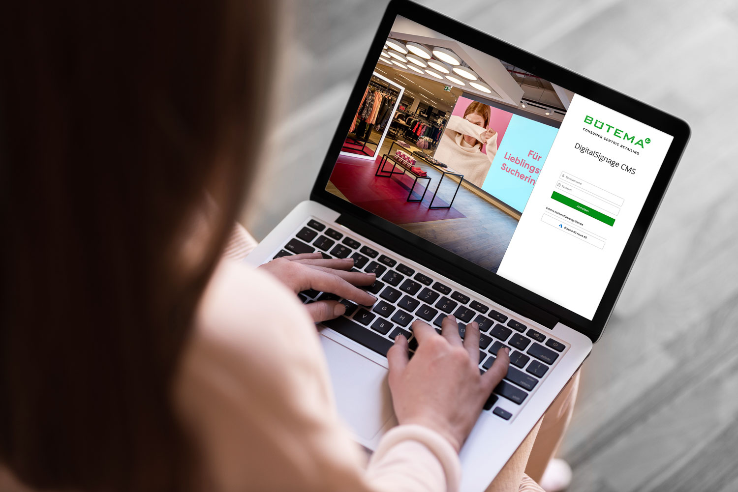 Person tippt auf einem Laptop, der eine Anmeldeseite für BÜTEMA Digital Signage CMS mit einem Ladenbild zeigt.