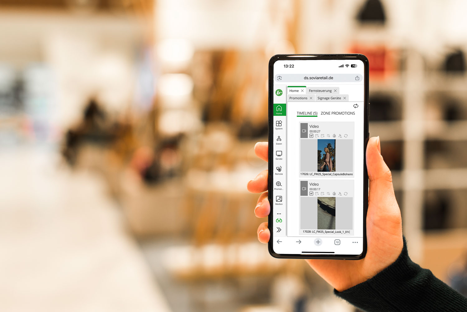 Hand hält ein Smartphone, das eine webbasierte Digital Signage Software mit Video-Playlist und Bedienmenü zeigt.
