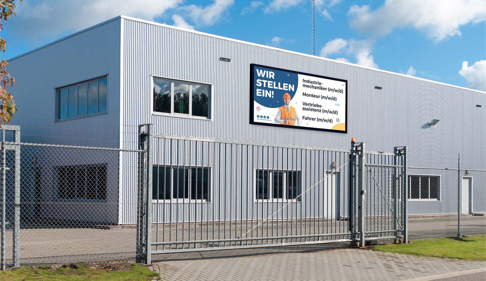 Industriegebäude mit einem Zaun davor und einem Schild, das auf Deutsch für Industriearbeiter, Monteure, Vertriebsassistenten und Fahrer Stellenanzeigen zeigt.