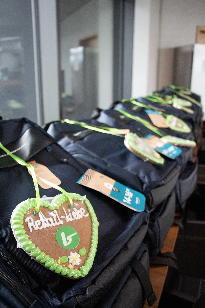 Mehrere schwarze Rucksäcke in einer Reihe mit herzförmigen Lebkuchenanhängern, auf denen ‚Retail-Liebe‘ steht.