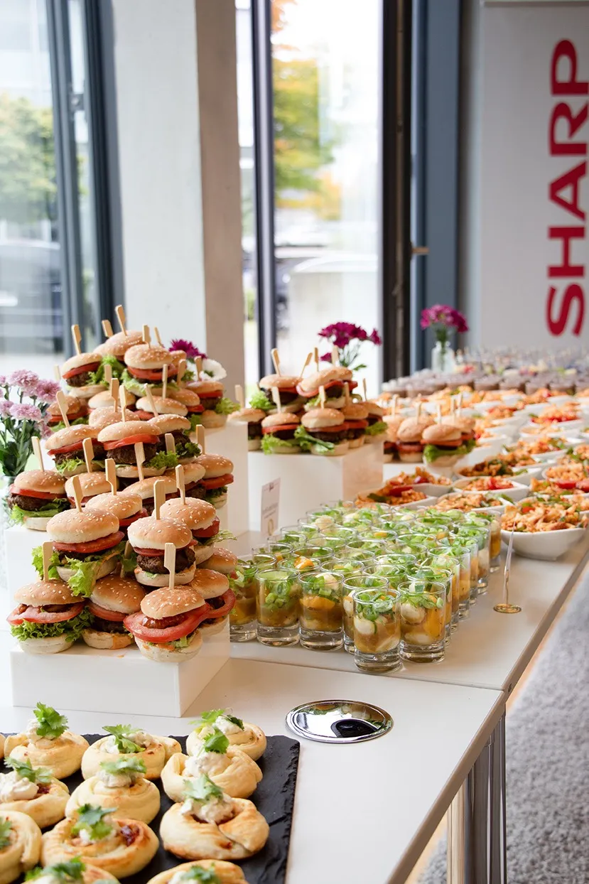Buffet-Tisch mit Mini-Burgern, kleinen Gläsern mit Avocado und Garnelen sowie herzhaften Blätterteig-Häppchen.