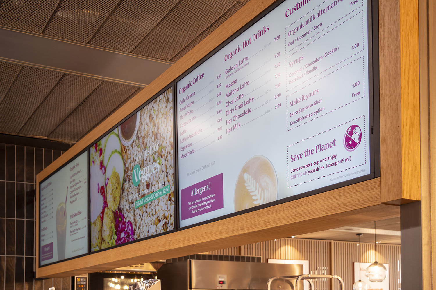 Digitales Menübrett in einem Café mit Angeboten für Bio-Kaffee, Bio-Heißgetränke, Milchalternativen und Sirupen sowie einem Umweltaufruf mit Rabatthinweis für wiederverwendbare Becher.