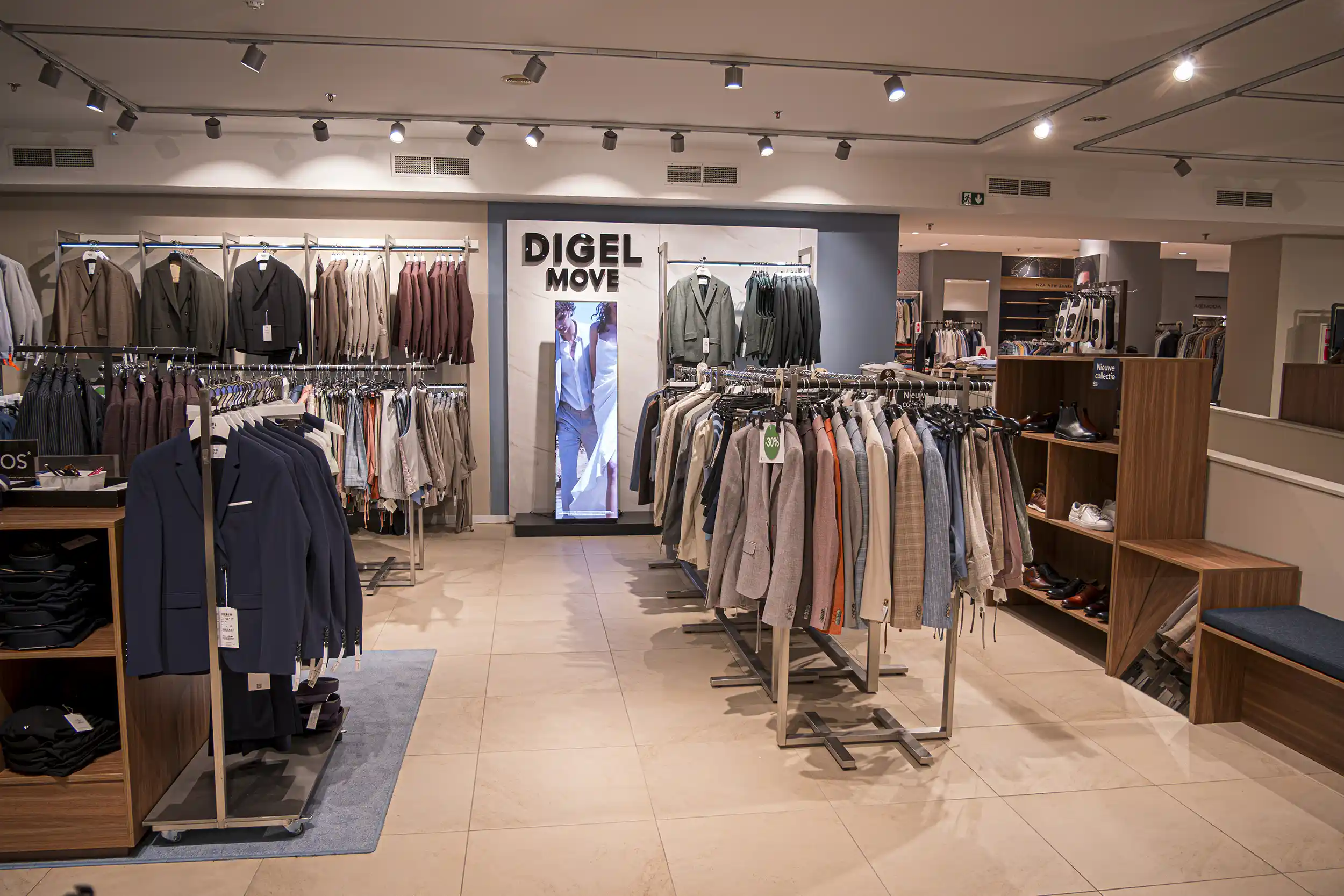 Moderne Herrenkleidungsgeschäft mit Anzügen, Jacken und Schuhen auf Ständern und Digital Signage Screens.