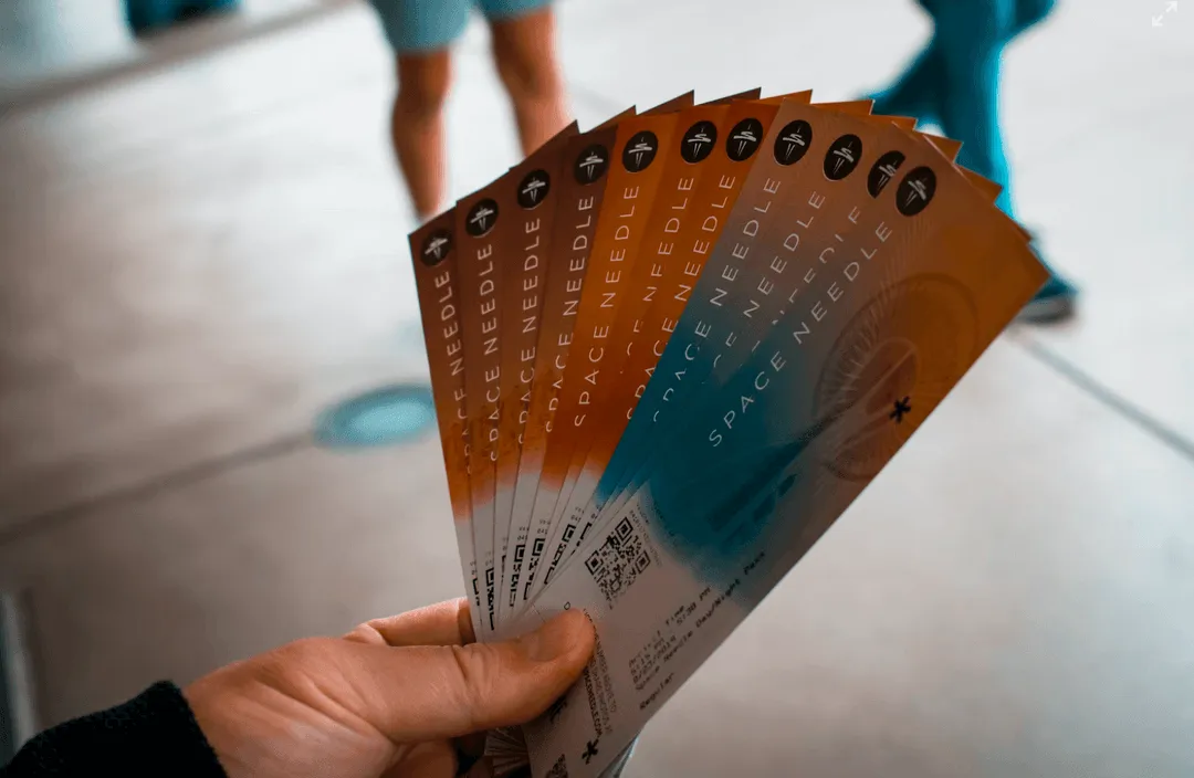 Hand holding a fan-shaped array of Space Needle tickets with blurred people in the background.