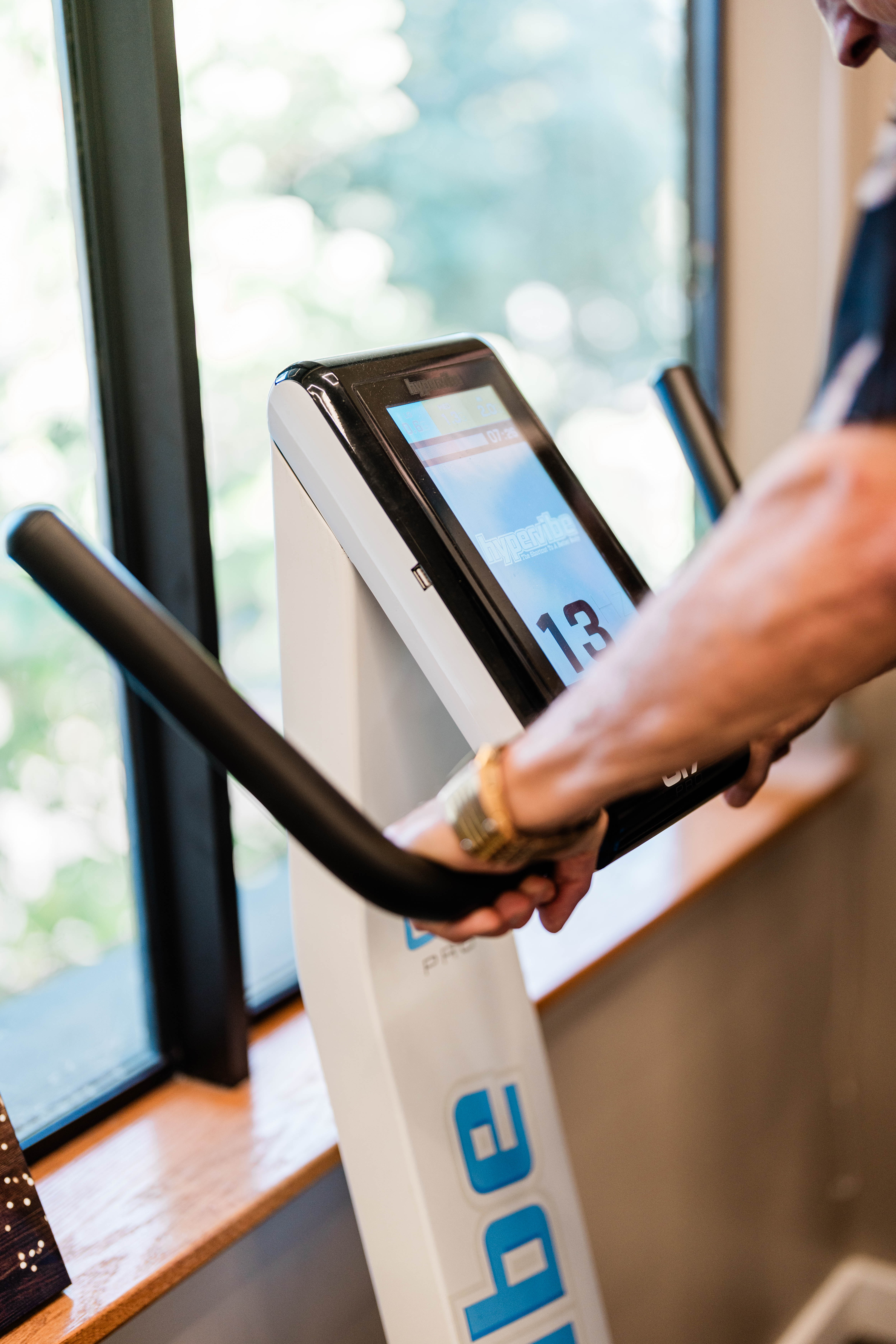 A close-up of a person's hands holding onto the handles of a hypervibe machine console, which is a tool used across many treatments, including Occupational Therapy, Physical Therapy, and Intensive Therapy.
