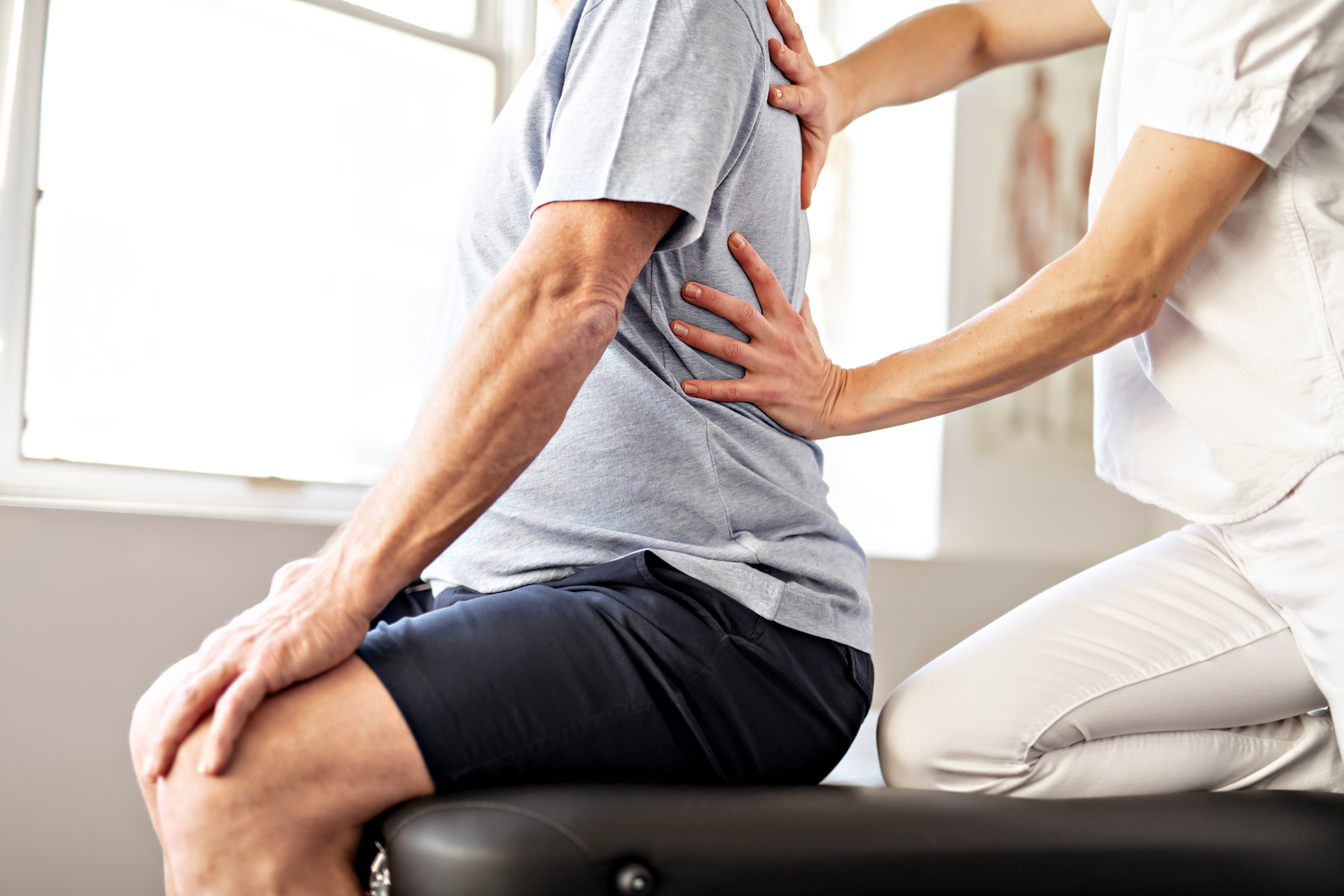 Chiropractor performing a back adjustment on a male patient sitting on a treatment table, illustrating a chiropractic treatment for spinal health.