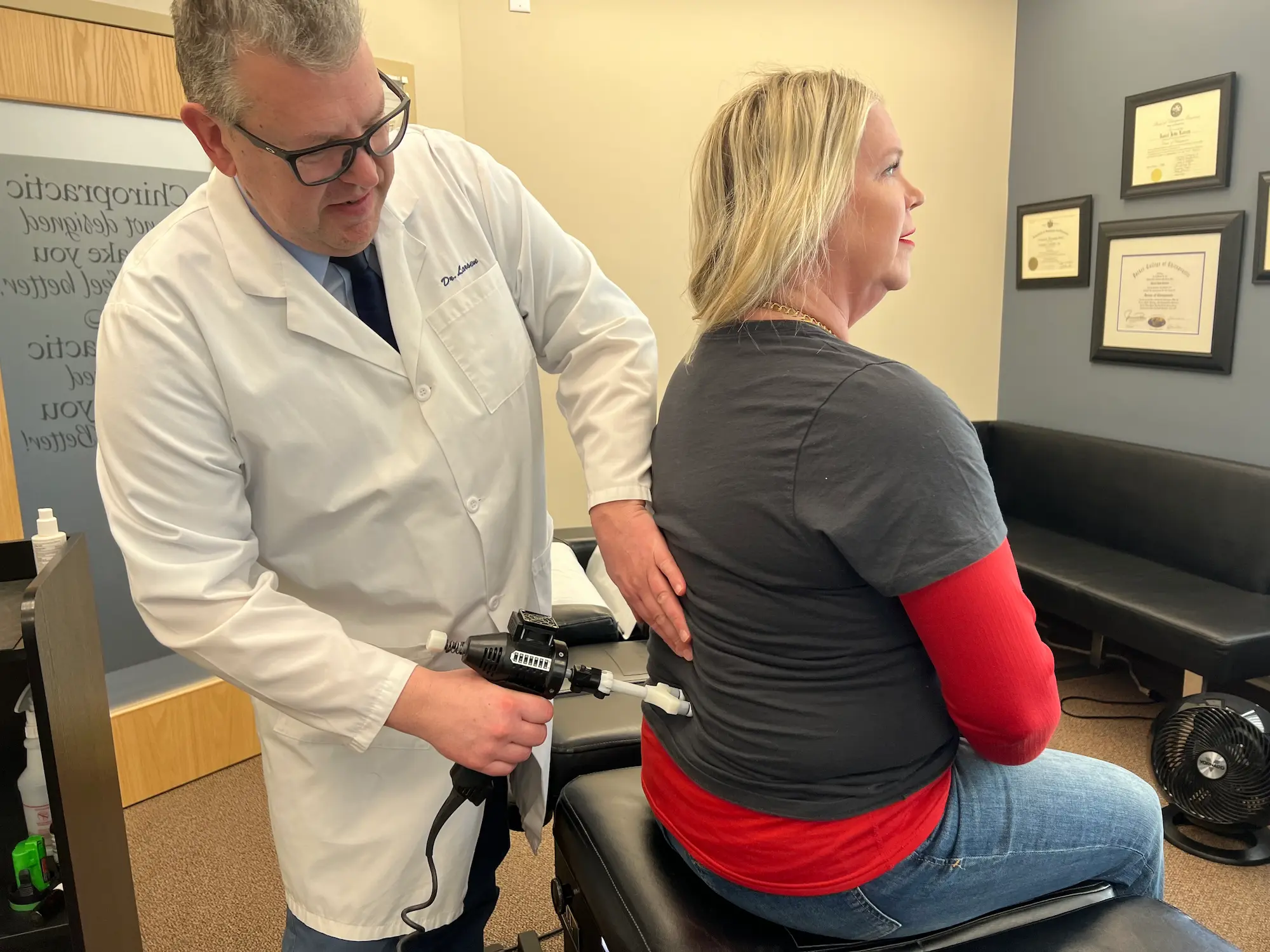 An advanced chiropractic treatment table featuring electronic controls and a screen, situated in a yellow-walled room with a clinical setup.