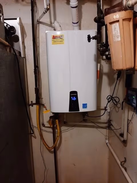 Wall mounted tankless water heater unit installed in a basement with pipes.