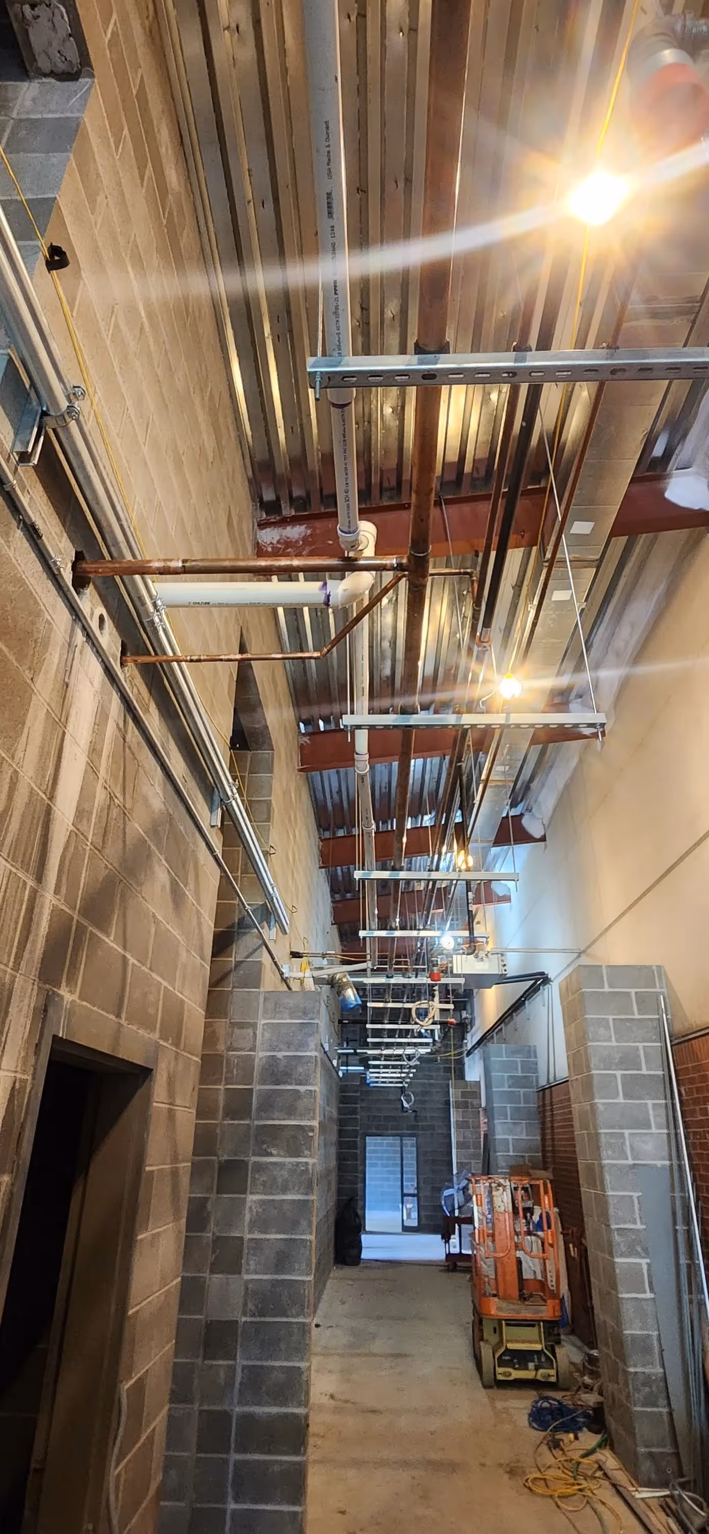 Newly installed rectangular HVAC ducts and pipes in an unfinished ceiling.