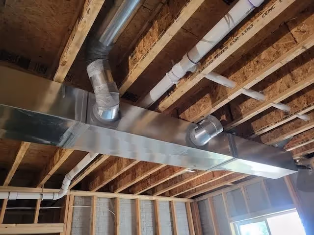 Newly installed rectangular HVAC ducts and pipes in an unfinished ceiling.