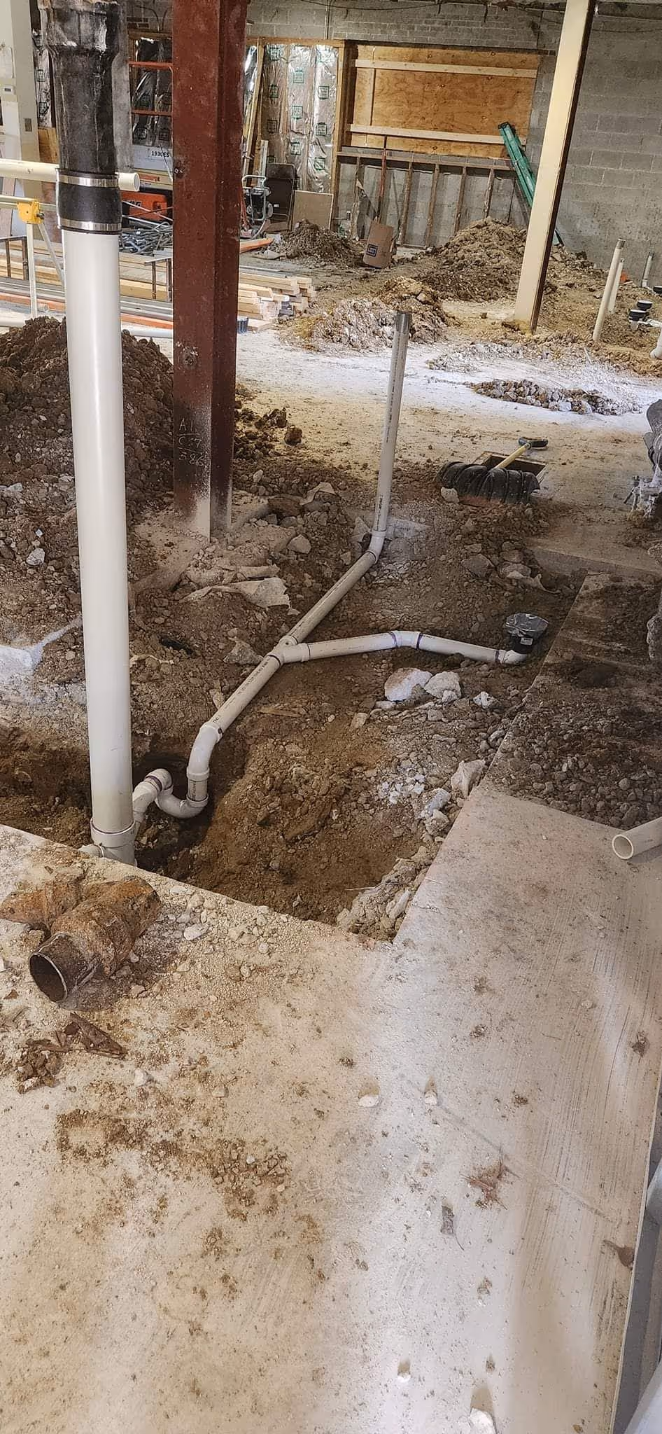 Construction trench with installed drain pipes and a plastic tub on soil.