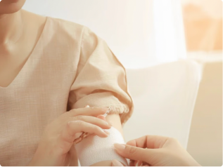 Close-up of a person applying a white adhesive bandage to another person's arm in a softly lit room.
