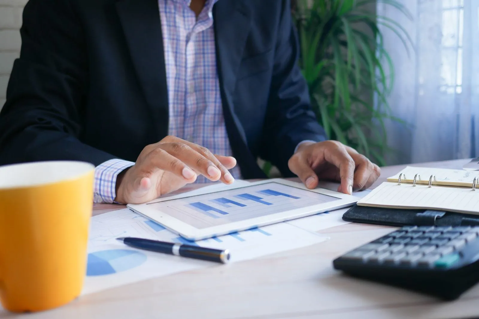 a photo of a sitting at a desk, which only shows the man's shoulders and hands. He is using an iPad that has a blue bar graph on it.