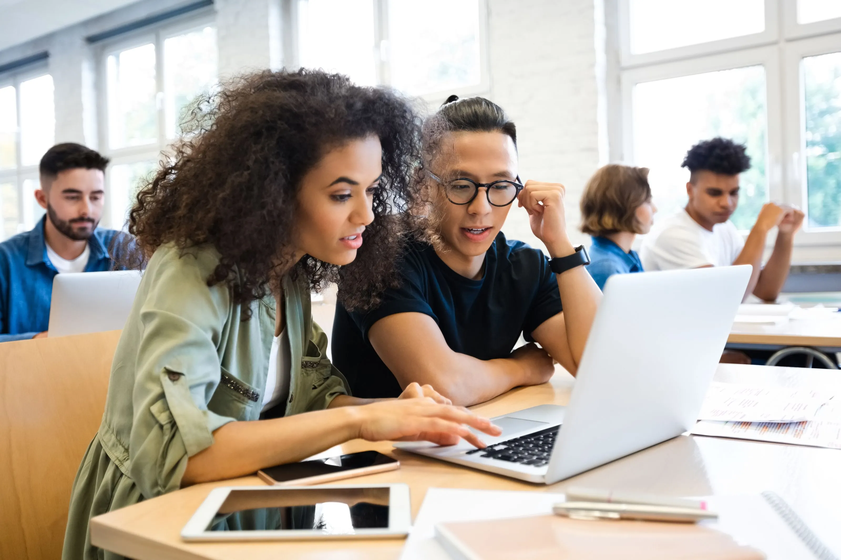 Two people sitting at a desk looking at a laptop together