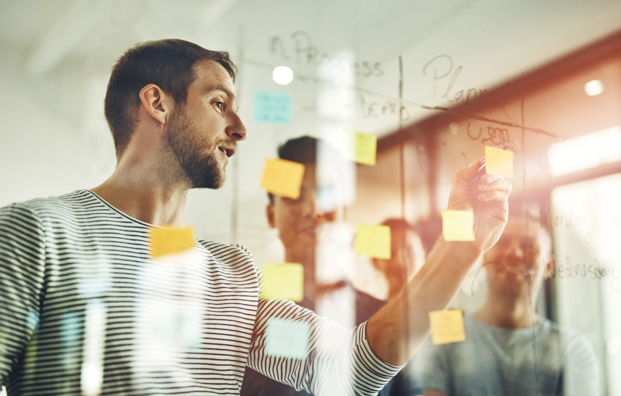 Man standing at a glass board placing sticky notes