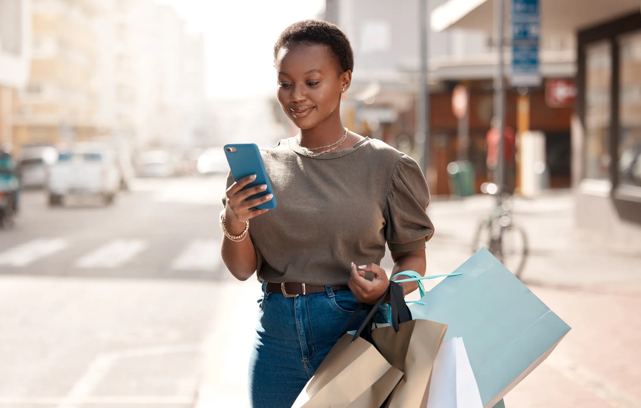 Person walking looking at a cellphone with shopping bags on her arm