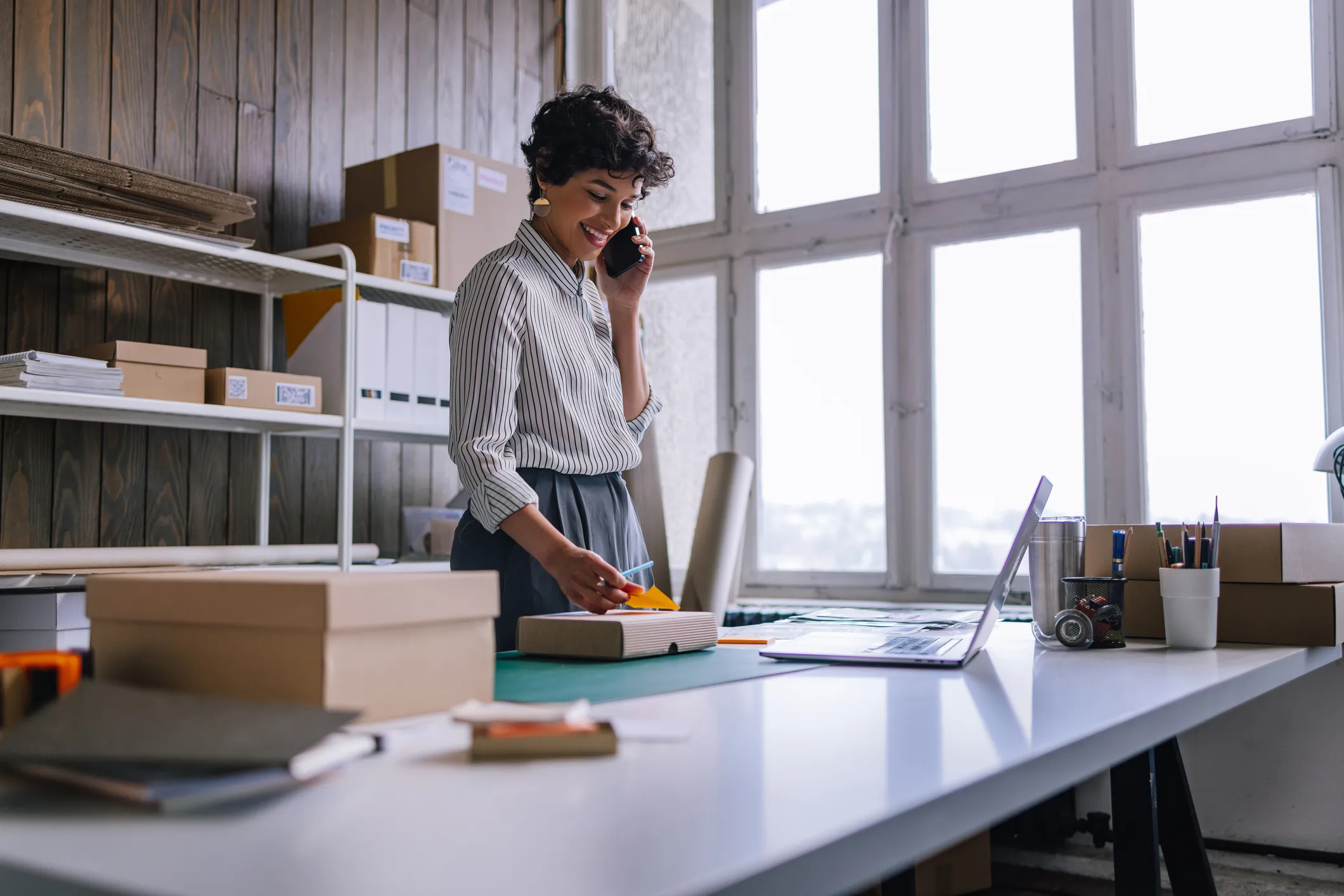 Women talking on the phone in front of a desk putting a sticky note on a box