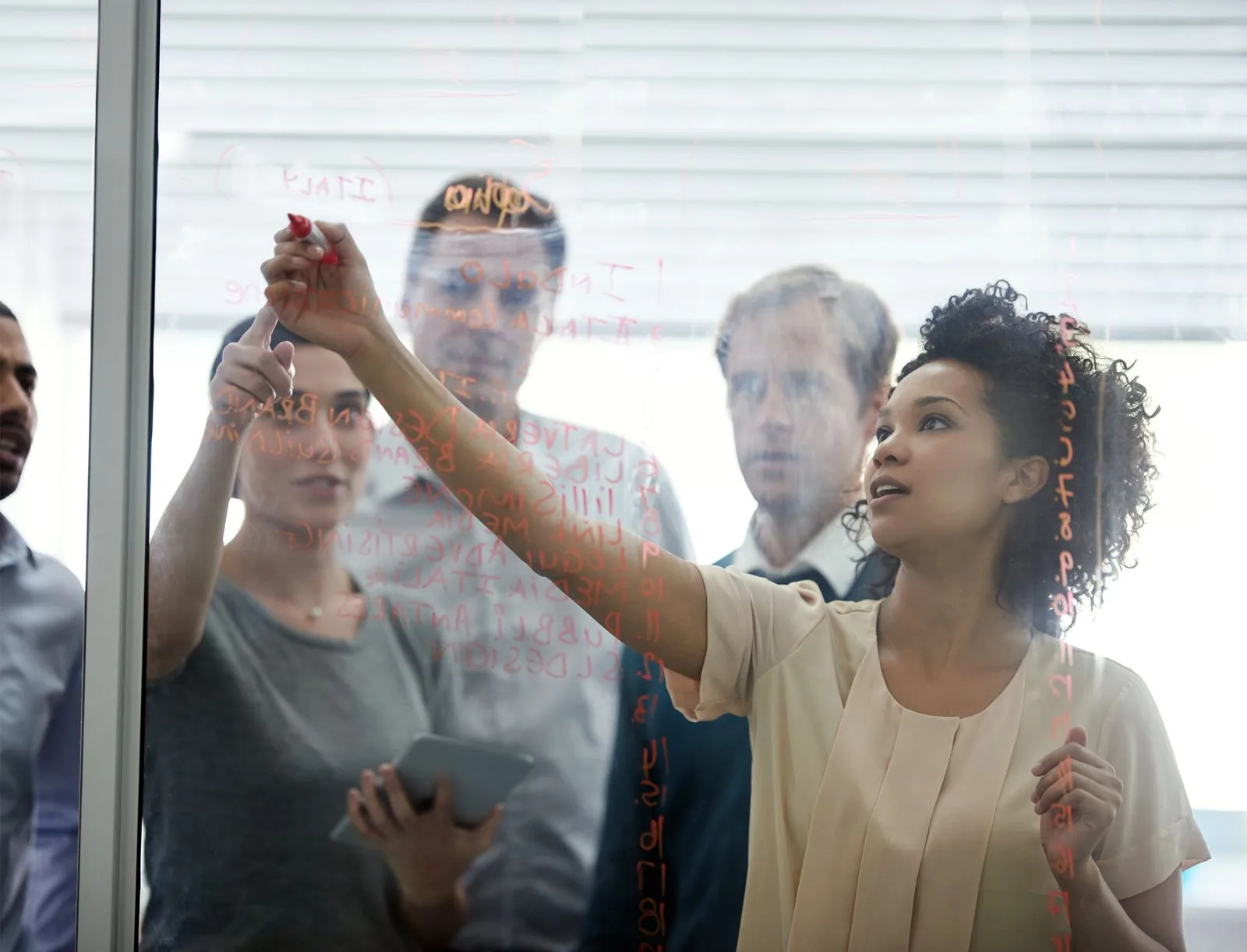 Woman writing on a dry erase board with colleagues behind her viewing