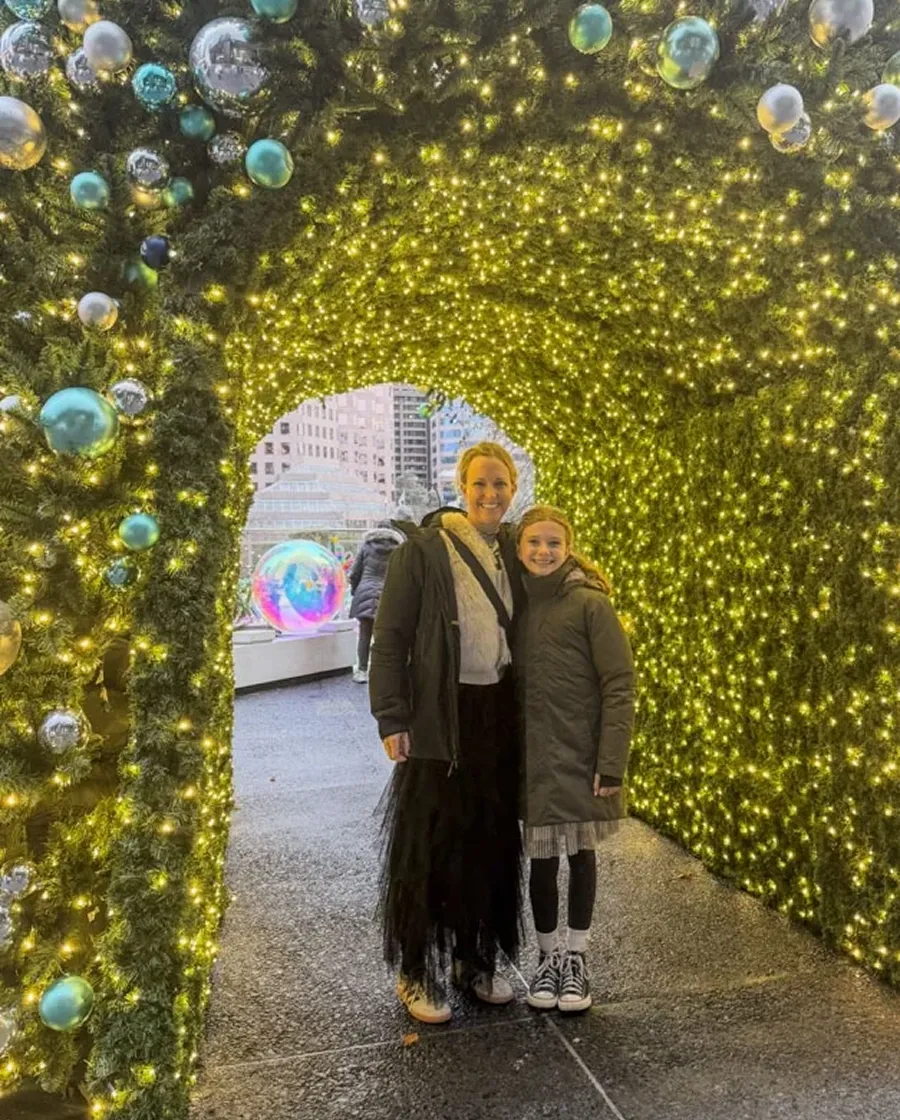 A mom and daughter under holiday lighting