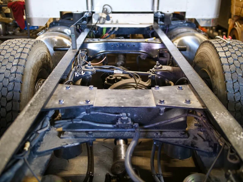 Suspension repair on a heavy-duty truck chassis with exposed drivetrain and rear axle components in service bay.