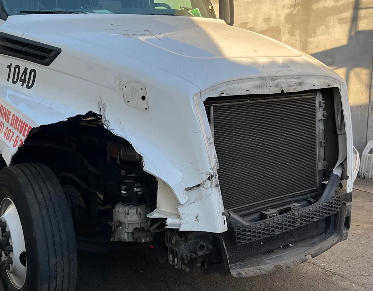 Collision repair for a heavy-duty truck with front-end damage and exposed radiator awaiting replacement parts.