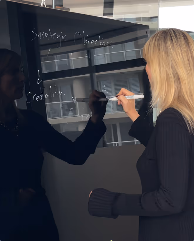 Professional woman writing strategic objectives on a glass board in a modern office, with reflections enhancing the visual depth. Key terms like “Credibility” and “Capability” highlight business planning, goal setting, and executive strategy sessions.