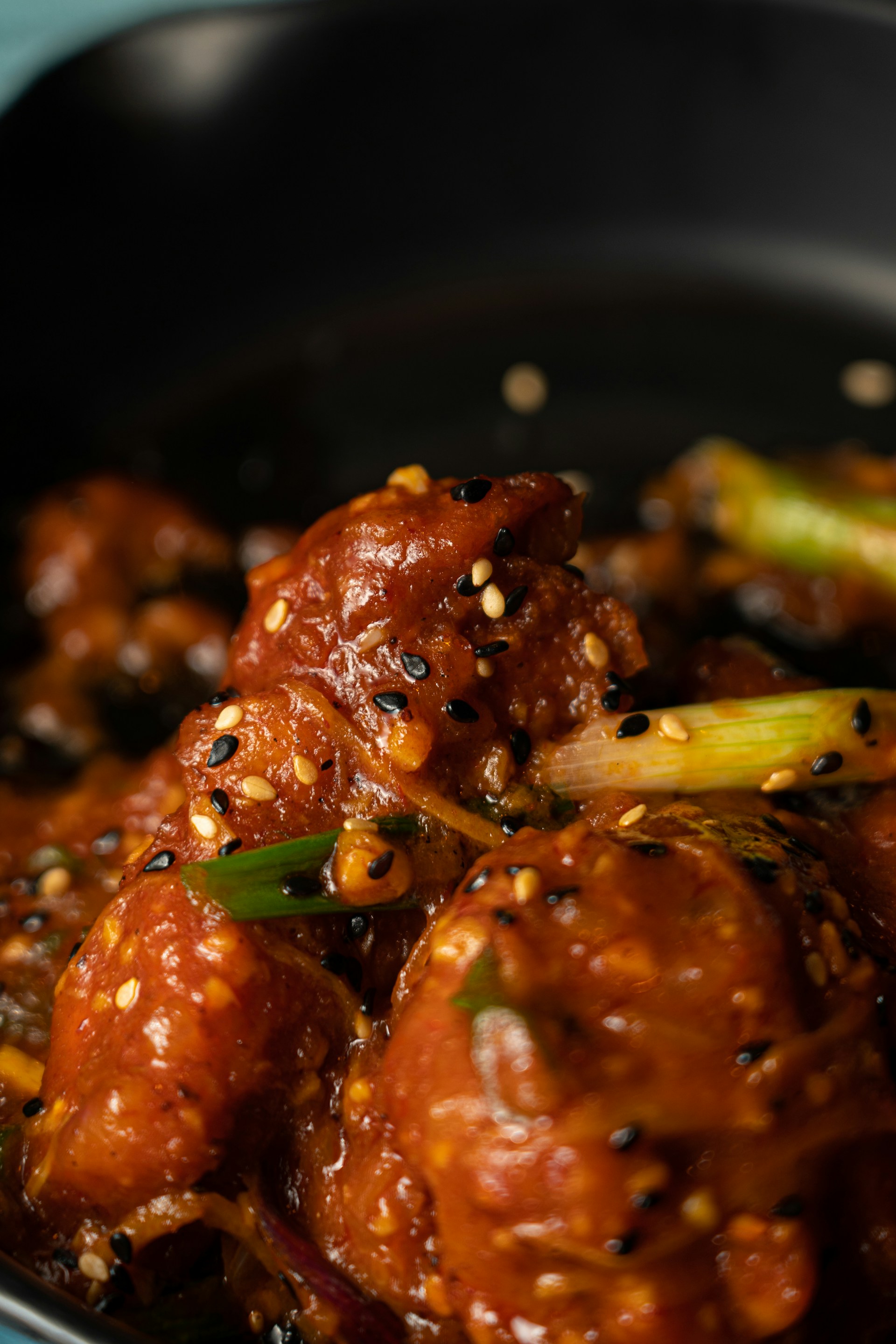 A bowl filled with chicken wings and vegetables, topped with sesame seeds