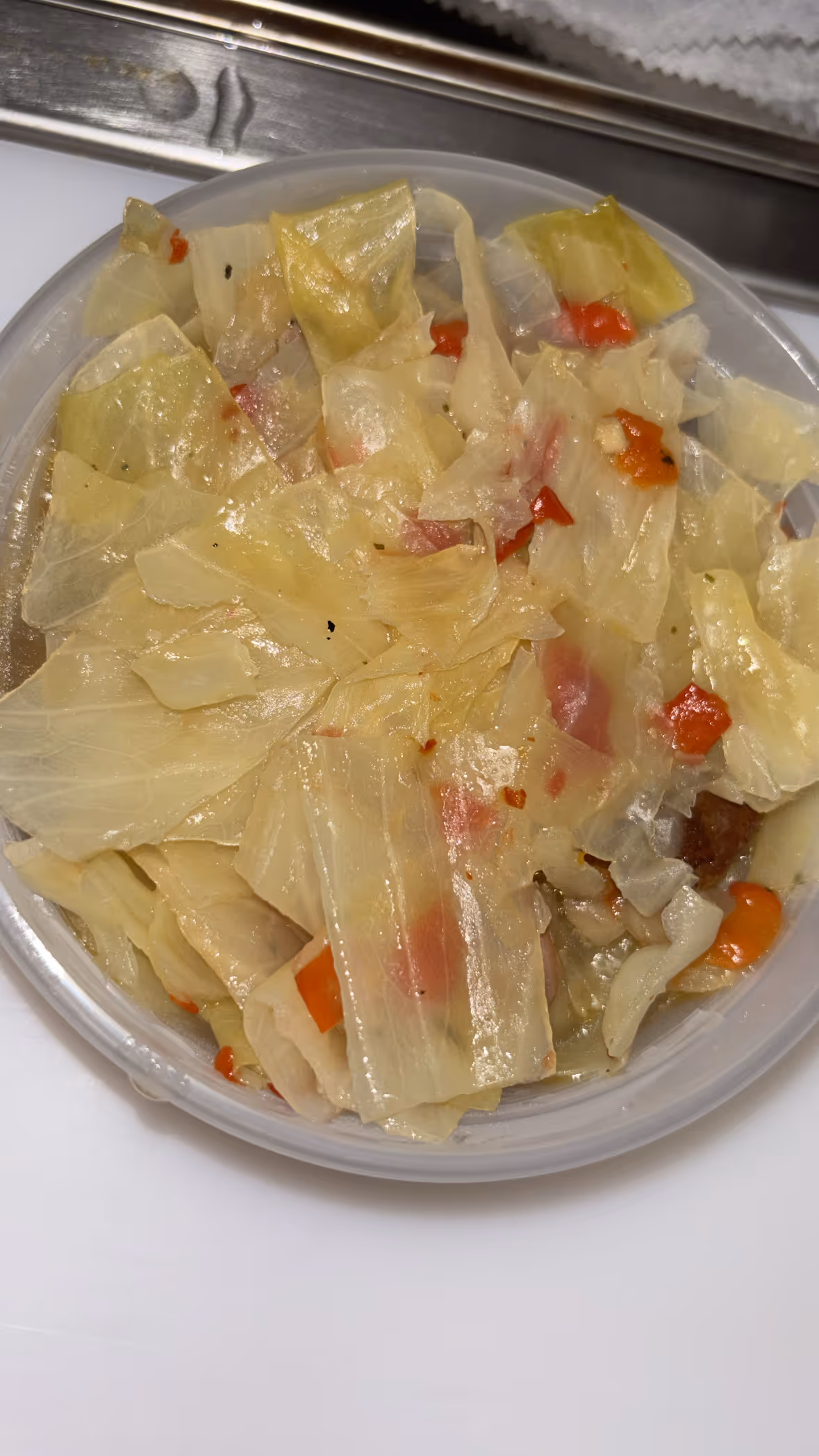 Close-up of cooked cabbage with diced red peppers served in a plastic container.