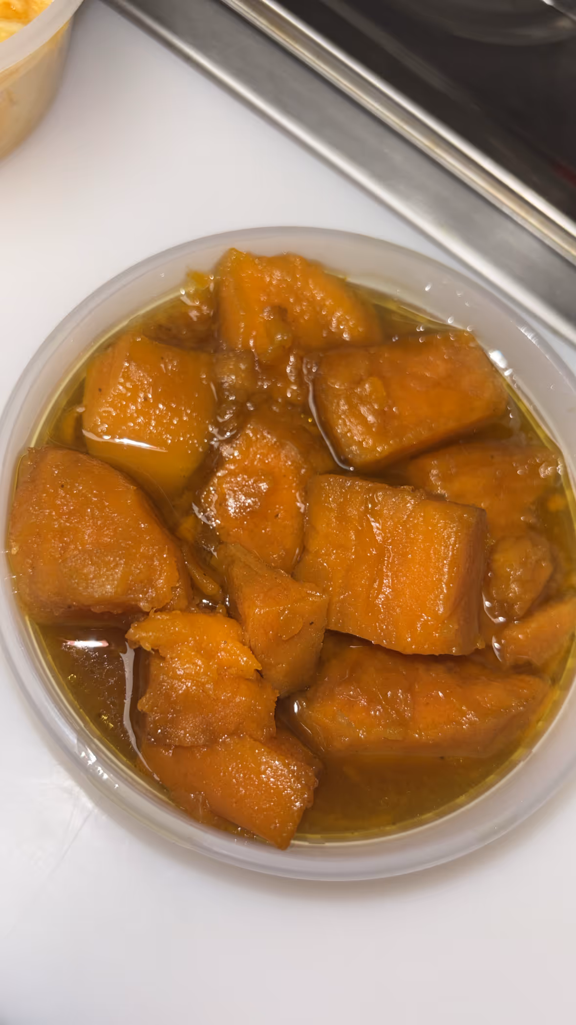 Close-up of sweet potatoes cooked in syrup in a small round plastic container.