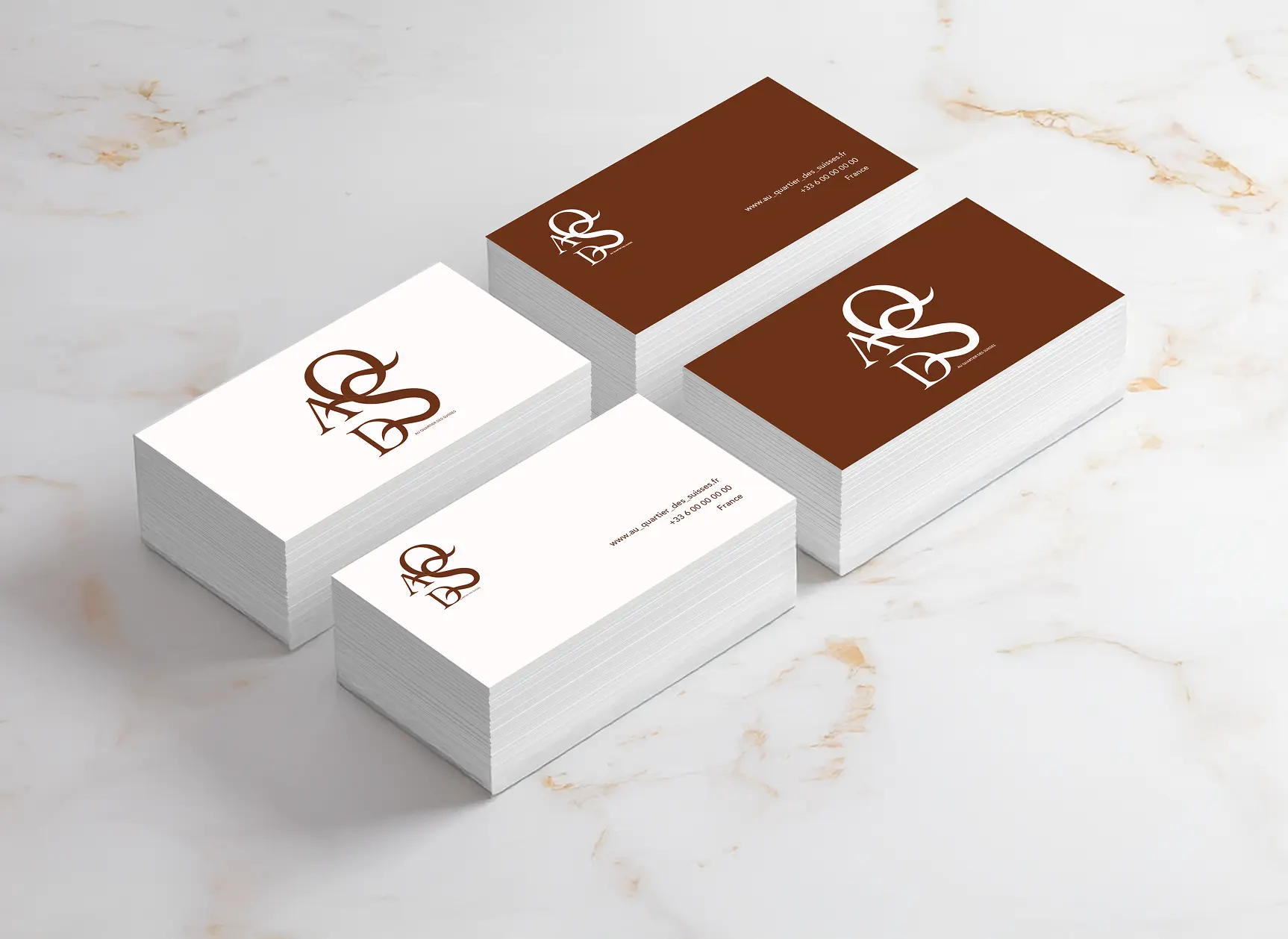 Stacks of brown and white business cards with a stylized 'QASD' logo and contact details on a marble surface.