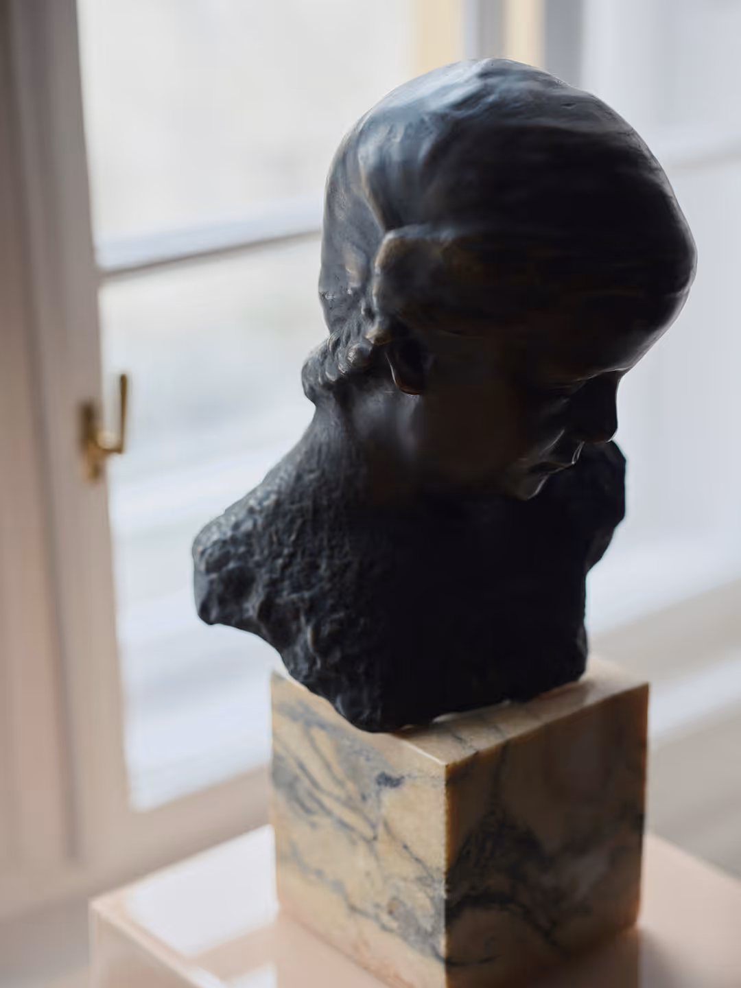 Szakállas férfit ábrázoló bronz mellszobor márványtalapzaton, az ablak előtt.