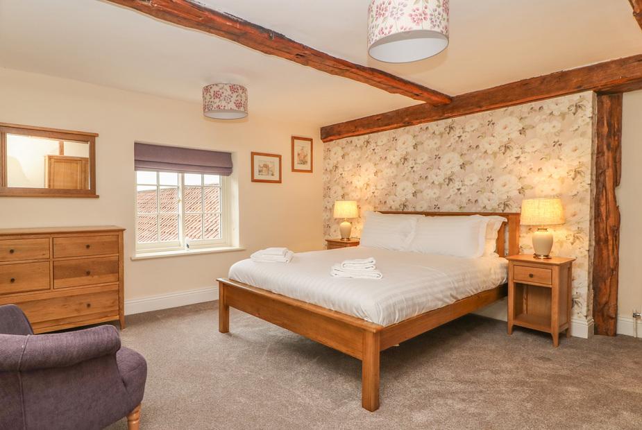 Cottage bedroom with double bed, floral wallpaper and exposed wooden ceiling beams