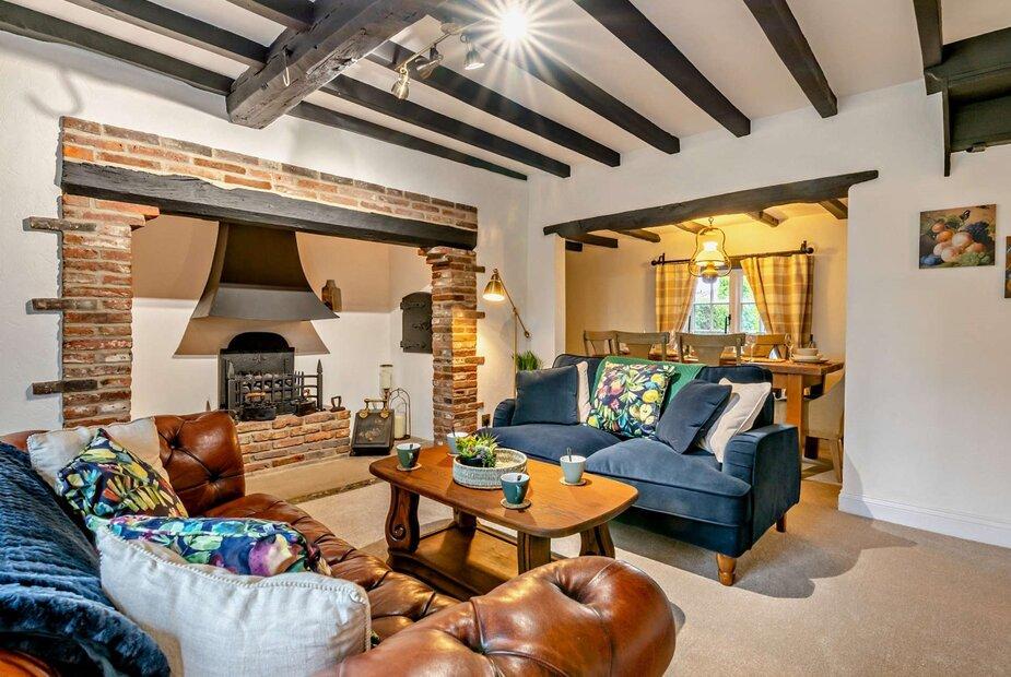 Cottage lounge with exposed beams, brick fireplace, sofas and view into dining area