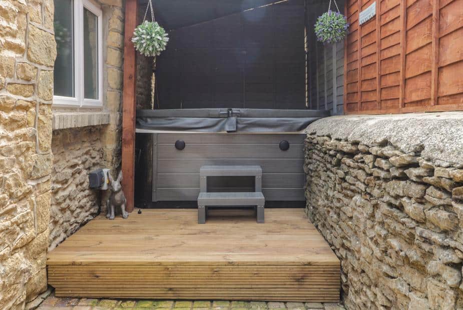 Cottage patio area with hot tub and wooden steps enclosed by stone walls