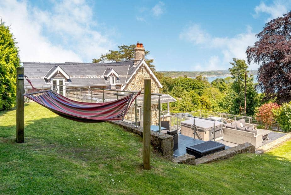 Hammock on lawn beside stone lodge with patio seating and hot tub