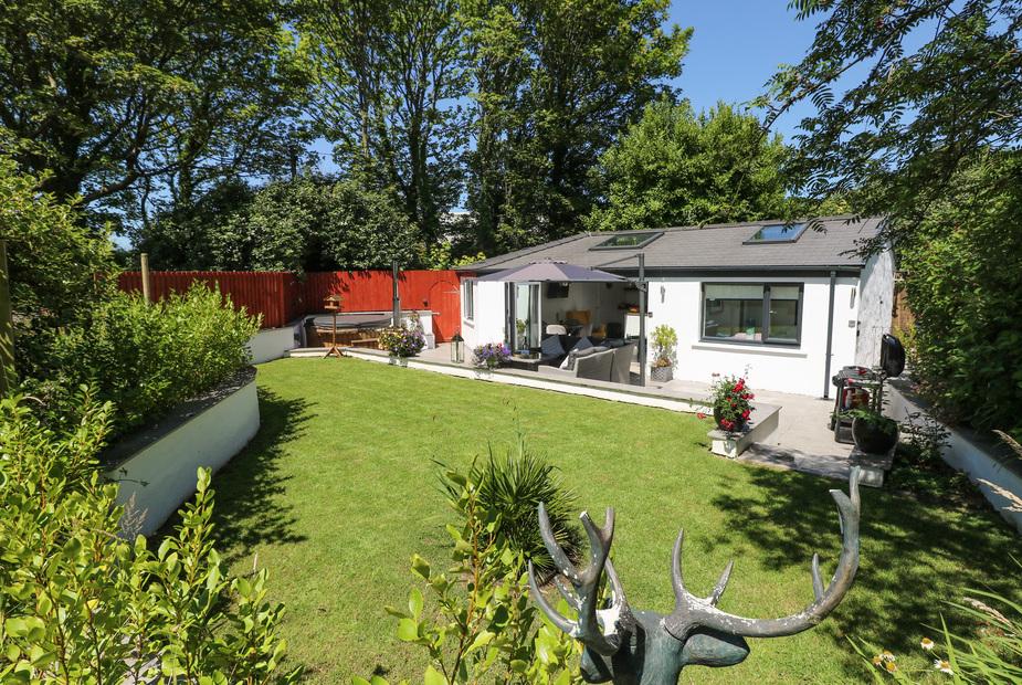 Summerhouse with patio seating, umbrella, and enclosed garden lawn surrounded by trees
