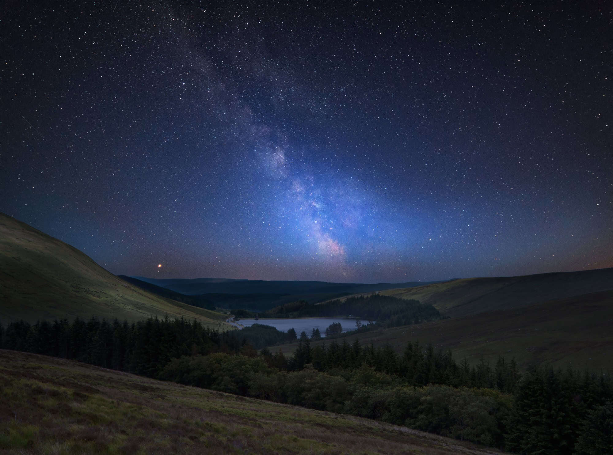 The Milky Way shining over a serene mountain lake in the Brecon Beacons Dark Sky Reserve.
