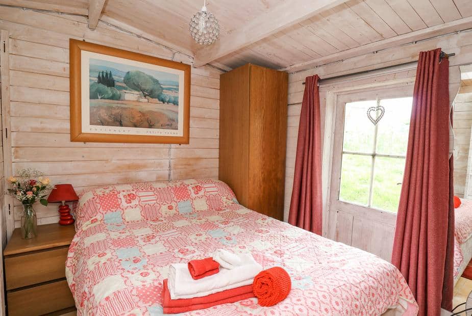 Lodge bedroom with double bed, bedside tables, wardrobe and door with red curtains